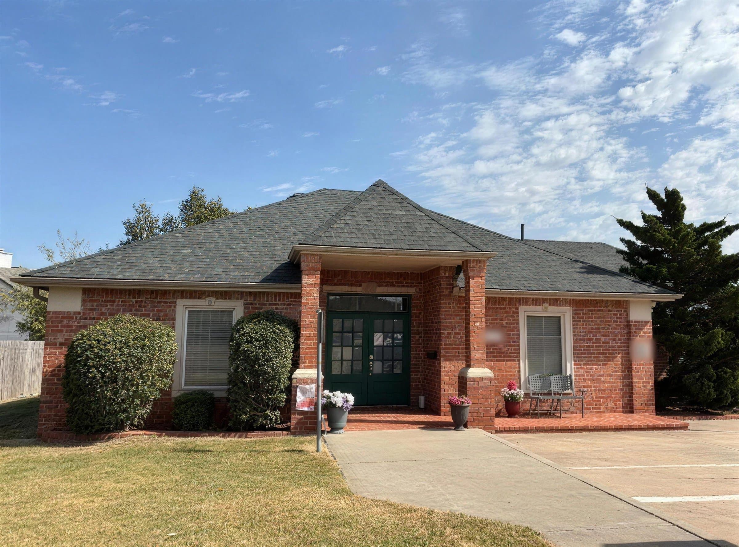 Red brick building with a new dark gray shingle roof under a blue sky